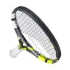 A close-up photograph of a tennis racket with a yellow grip and a white string bed, lying on a blue court with visible tennis balls in the background